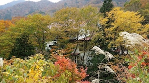 A mountainous landscape with autumn foliage, a traditional building with a red roof, and a river in the background. - Tenjin Lodge (Minakami)