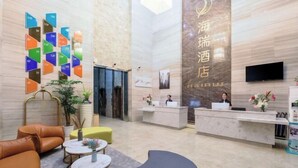 A hotel reception area with a modern design, including a reception desk, seating area with sofas and tables, and a wall with colorful nameplates. - Hairui Hotel (Chongqing)