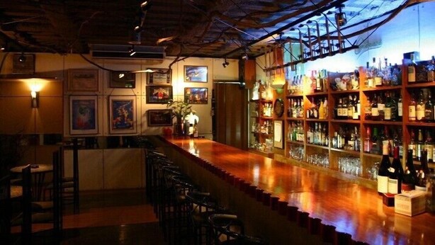 A bar area with a wooden counter, bar stools, and shelves stocked with bottles. - Hotel Fukuya (Takamatsu)