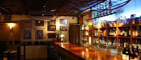 A bar area with a wooden counter, bar stools, and shelves stocked with bottles.