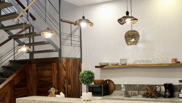 Una cocina con una isla de madera, taburetes de bar, una planta y una escalera.