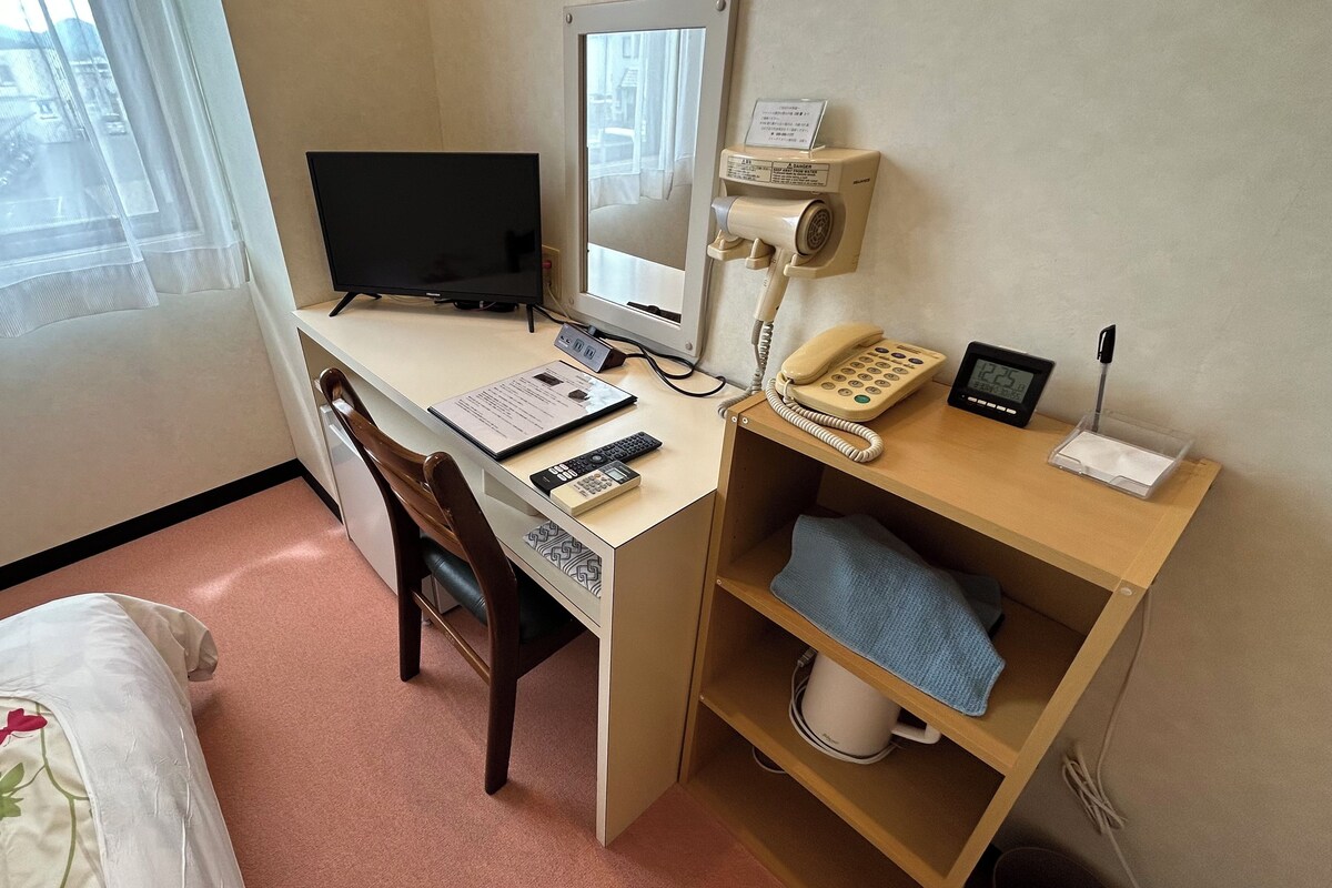 Une chambre d’hôtel équipée d’un bureau, d’un ordinateur, d’un téléphone et d’une petite étagère sur laquelle se trouve une serviette.