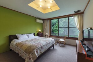 A hotel room with a bed, a desk, a chair, a window with a view of trees, and an air conditioning unit.