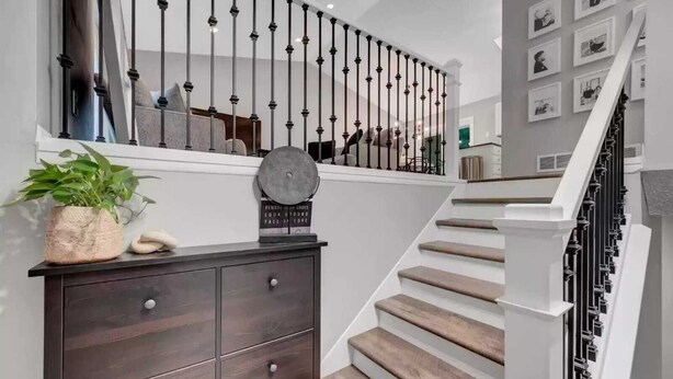 A staircase with wooden steps and a black railing, a dark wooden dresser with drawers, and a potted plant.