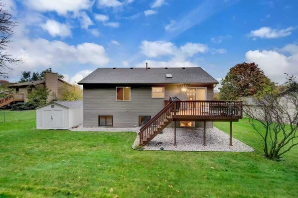 Ein zweistöckiges Haus mit einer Terrasse und einem kleinen Gartenhaus im Hinterhof.