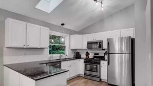 A modern kitchen with white cabinetry, a black countertop, stainless steel appliances, and a skylight.