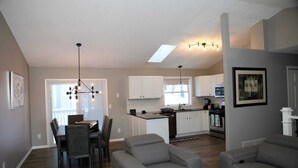 A modern kitchen with white cabinets, a dining area with a table and chairs, and a living room with two sofas and a coffee table.
