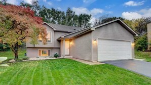A two-story house with a garage, a well-maintained lawn, and a tree with autumn foliage.