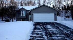 Ein zweistöckiges Haus mit Garage, umgeben von schneebedecktem Gelände und Bäumen.