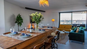 A modern dining area with a wooden table set for four, a vase of flowers, and a city view through large windows.