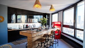 A modern kitchen with a central island, bar stools, and large windows offering a city view.
