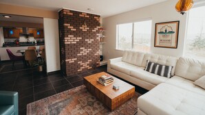 A modern living room with a white sofa, a wooden coffee table with books, a patterned rug, and a brick accent wall.