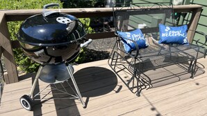 En grill på ett trädäck, tillsammans med en metallstol och en kudde med texten ”Hundar är välkomna”.