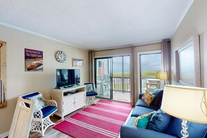 Relax in a cozy seating area with a sofa and wicker chair, perfect for unwinding with a flat-screen TV and balcony views.