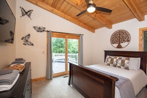 Ein Schlafzimmer mit Holzbalkendecke, einem Bett mit gemusterten Kissen, einem Schminktisch und Wandbildern mit Schmetterlingen.