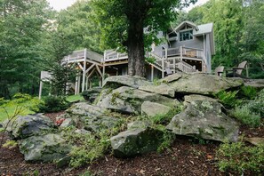Escape to a secluded forest retreat with a rustic lodge featuring a balcony overlooking the surrounding greenery and a unique tree trunk design.