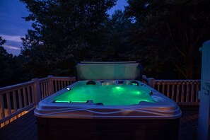 Ein Whirlpool mit Holzterrasse und Geländern, umgeben von Bäumen.