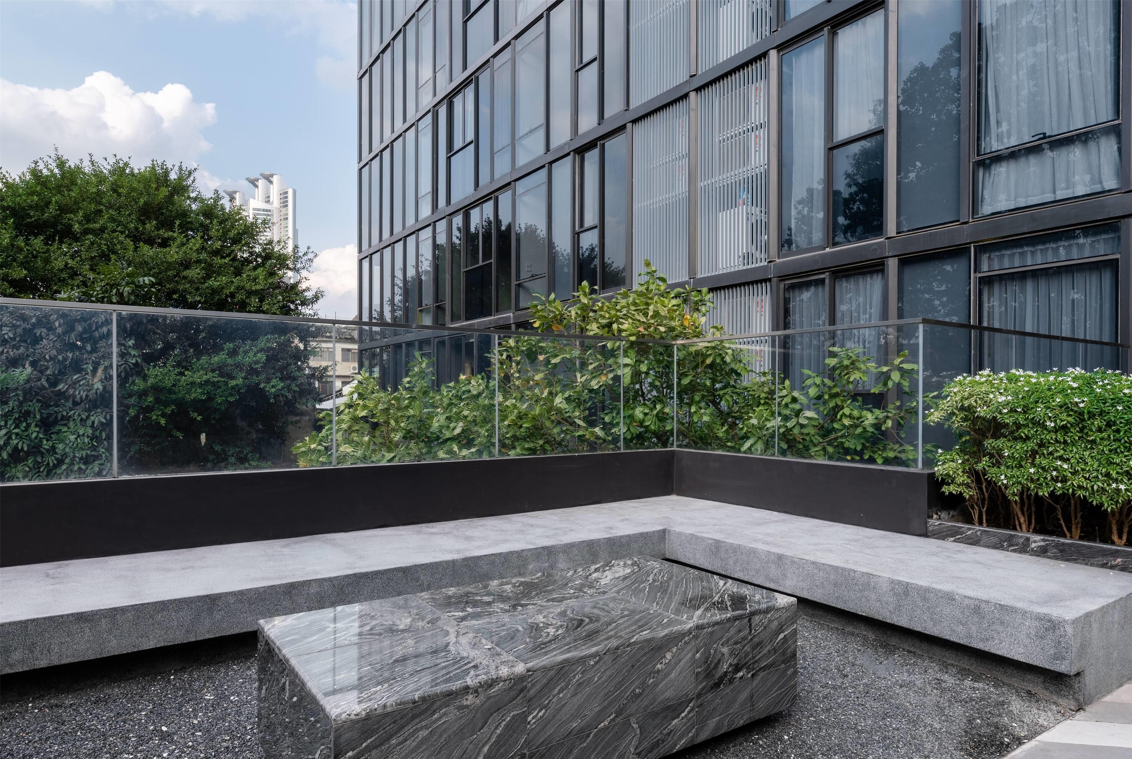 A modern outdoor seating area with a marble bench and a glass railing overlooking a cityscape.