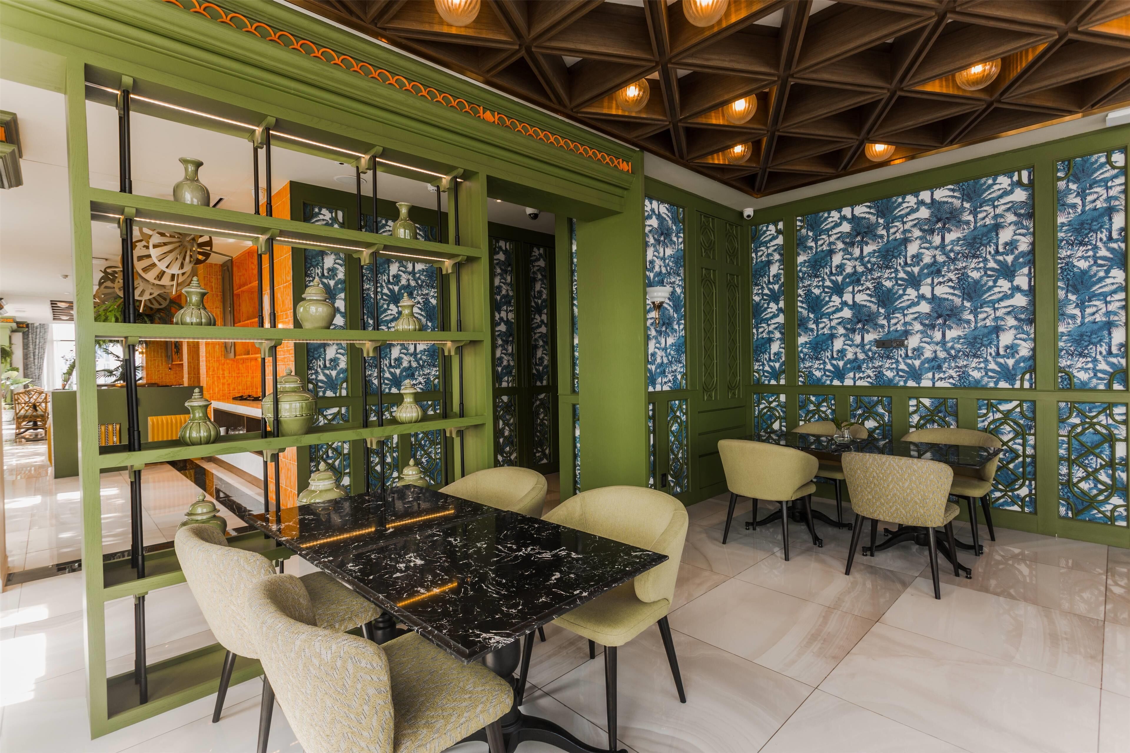 A dining area with a black marble table and beige chairs, surrounded by green walls with decorative panels and a patterned wallpaper.