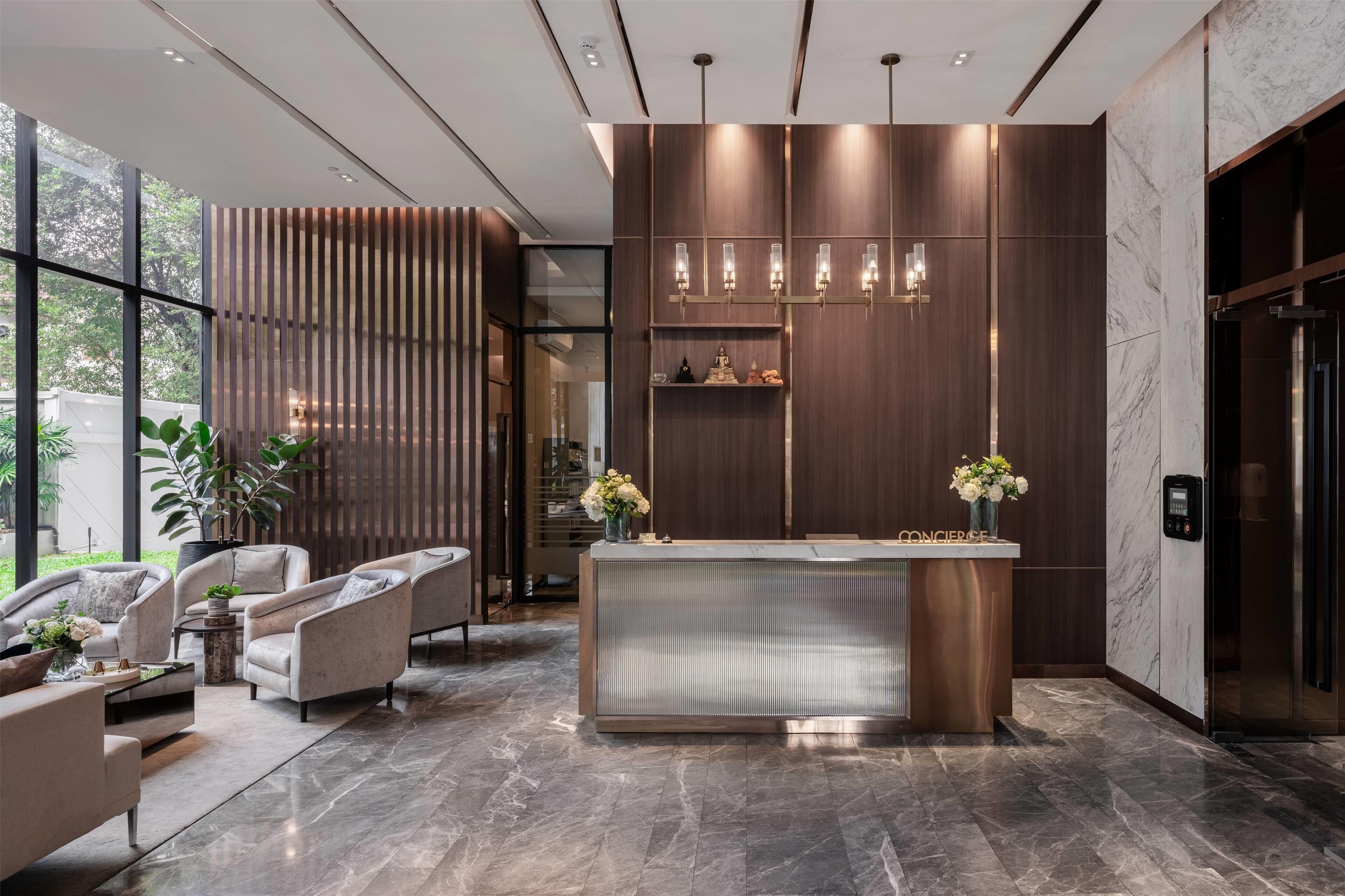A modern lobby with a reception desk, seating area, and a large window offering a view of greenery.