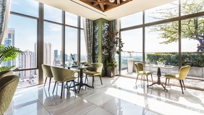 Ein moderner Essbereich mit großen Fenstern, Blick auf die Stadt und einer Wand in Grüntönen.