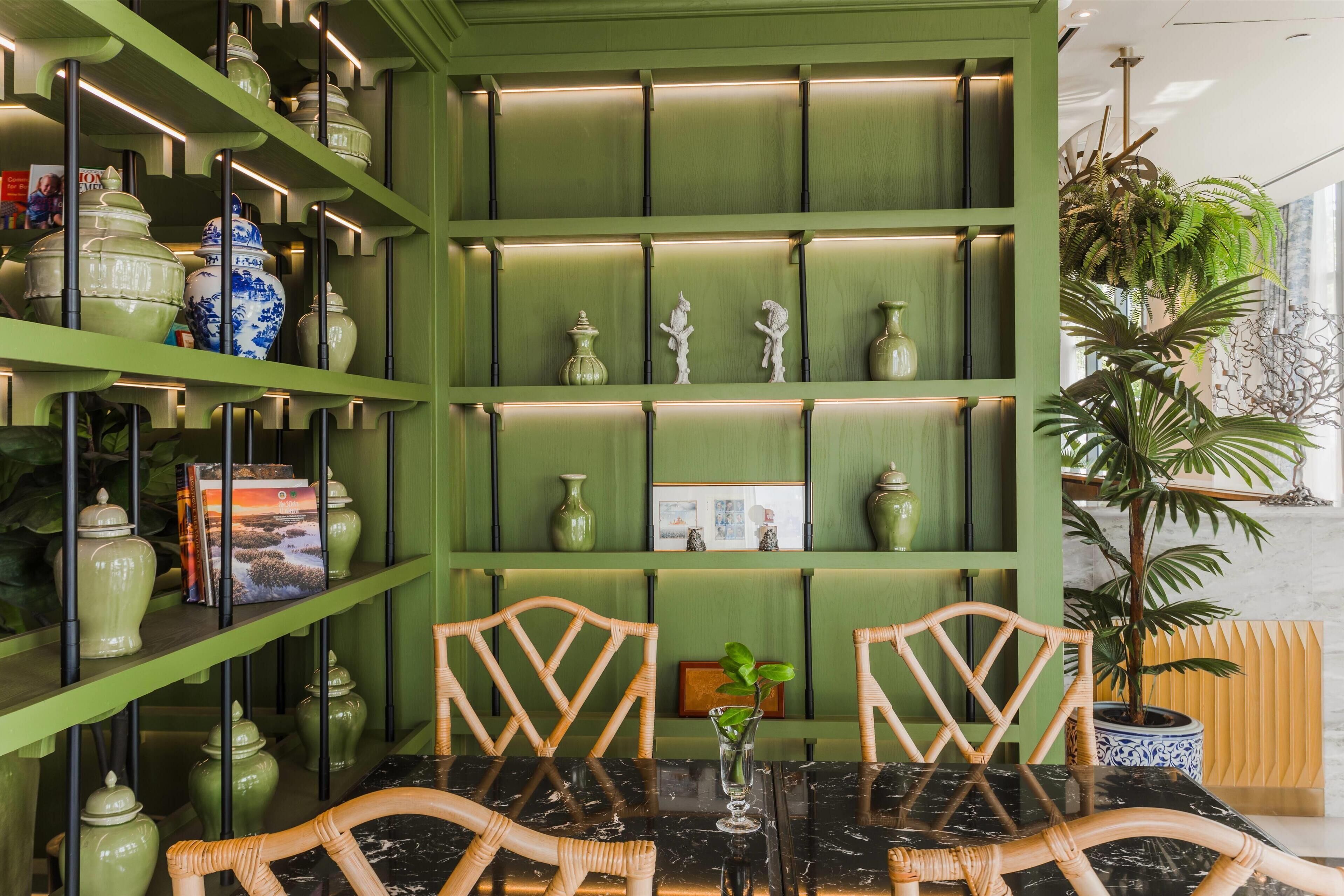 A green-themed room with shelves displaying ceramic vases and a dining table with chairs.