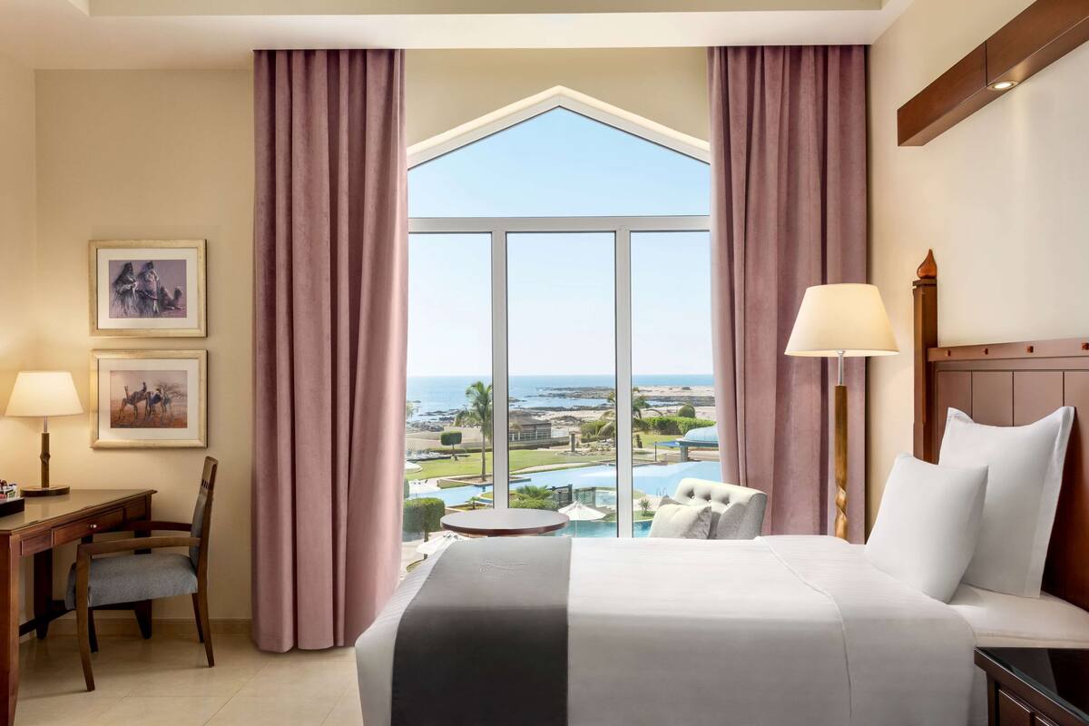 Habitación de hotel con una cama grande, un escritorio, una silla, una mesa redonda y vistas a un resort y al océano.