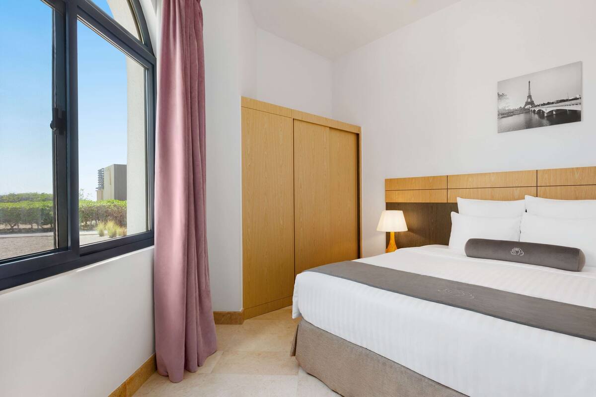 Habitación de hotel con una cama, un armario de madera, una ventana con cortinas, una lámpara y un cuadro en la pared de la Torre Eiffel.