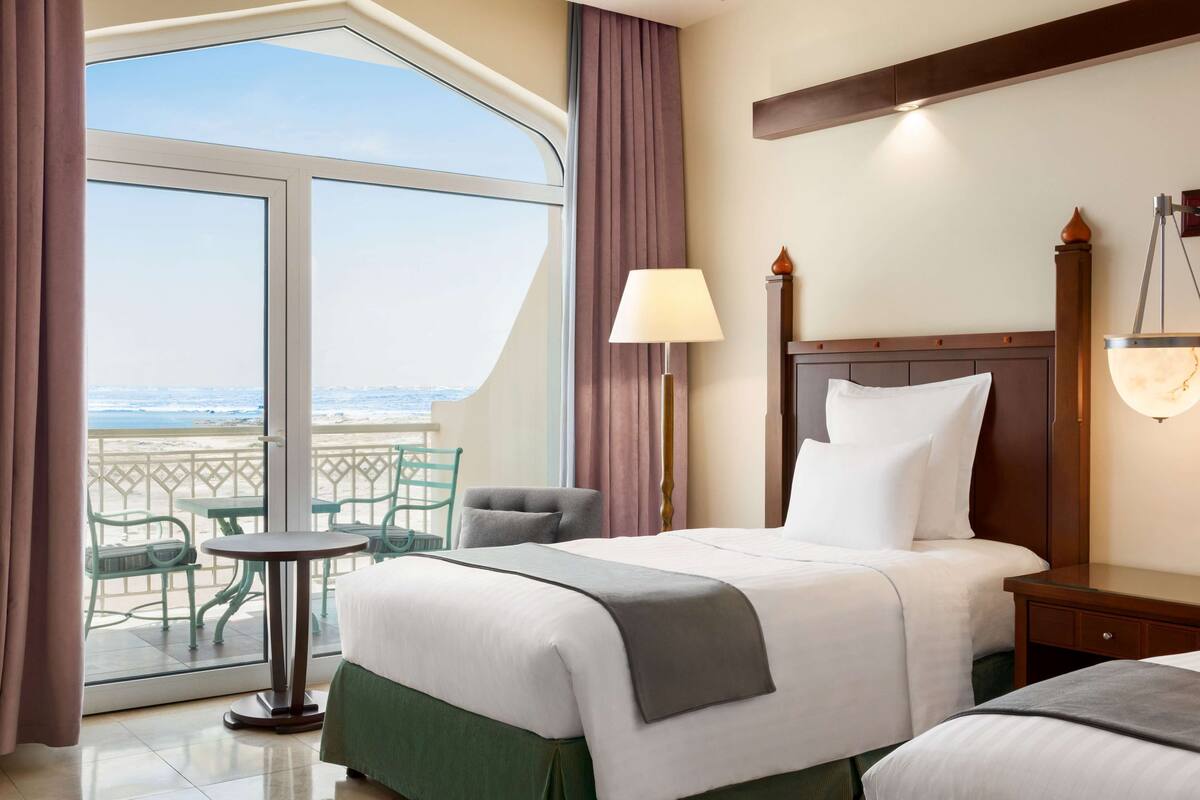 Una habitación de hotel con un ventanal grande, una cama, una silla, una mesa y una lámpara.