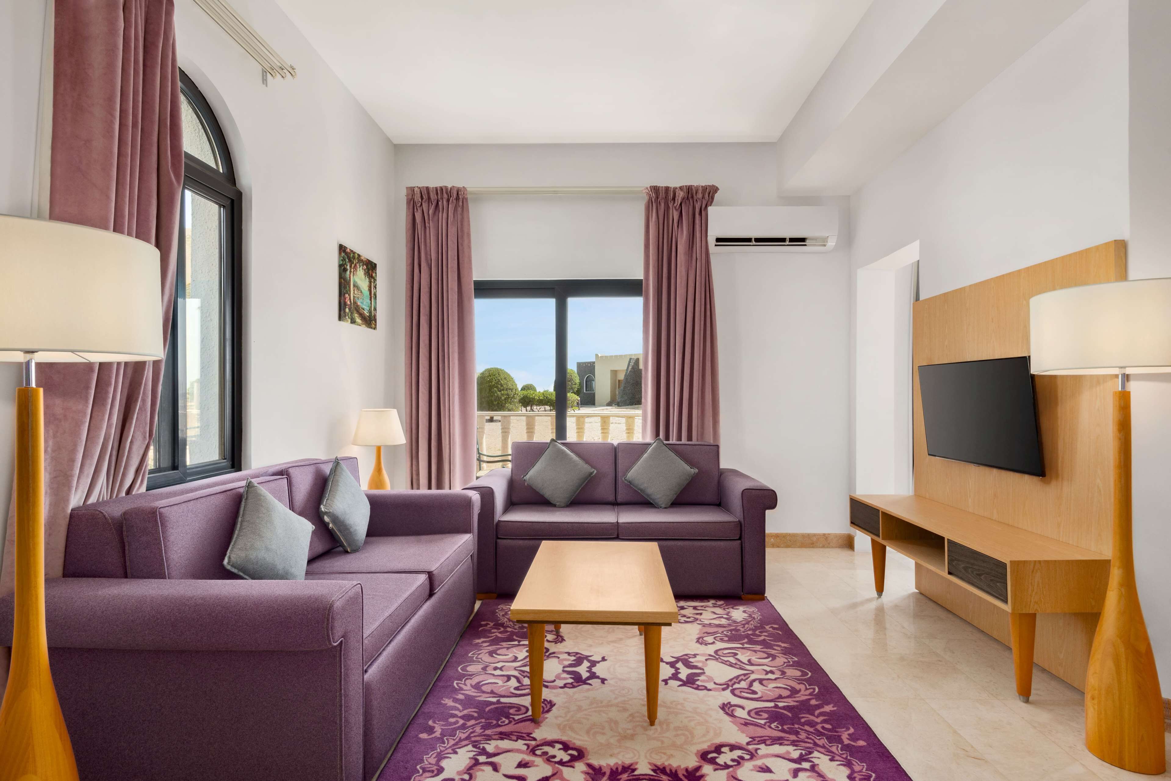 A modern living room with a purple sofa set, a wooden coffee table, and a TV on a wooden stand.