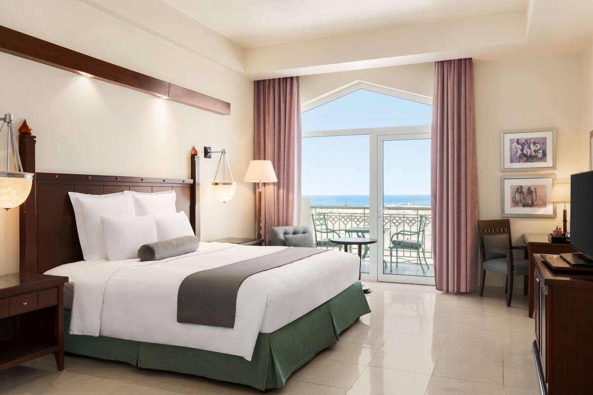 Una habitación de hotel con una cama grande, un escritorio, una silla, un balcón y vista al mar, además de un televisor.