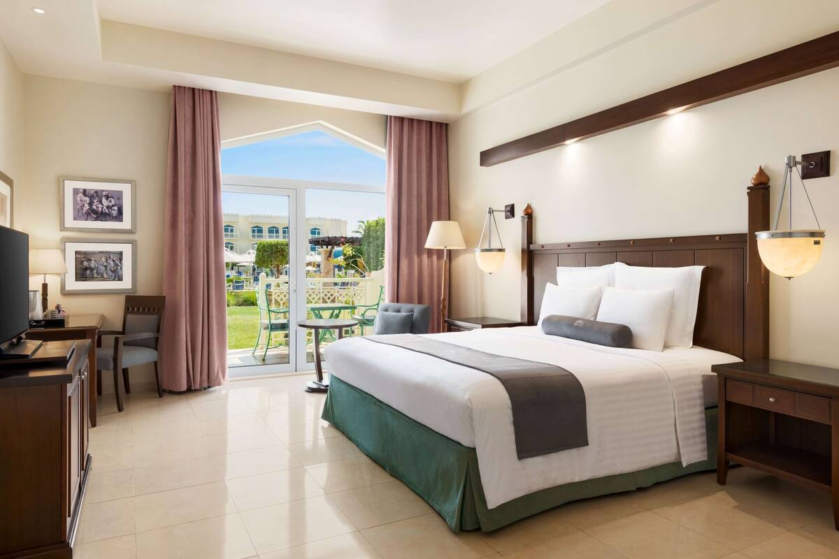Habitación de hotel con cama, escritorio, silla, televisión, lámpara y vistas al exterior.