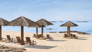 Una playa con sombrillas de paja y sillas reclinables.