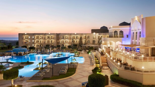 Un hotel con una gran piscina, zonas de estar al aire libre y una fachada de edificio bien iluminada.