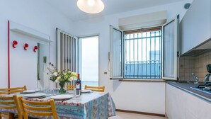 Un comedor con una mesa dispuesta para cuatro, sillas de madera, un florero con flores y una ventana con barrotes.
