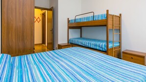 Ein Schlafraum mit Etagenbett, einem gestreiften Bettbezug, Holzmöbeln und einem Holzschrank.