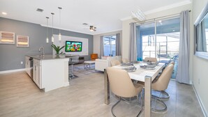 A modern kitchen with a central island, a dining area with a large table and chairs, and a living space with a TV and seating. - FA4381 Storey Lake Home 4Beds 3baths Private Pool and Free Waterpark (Kissimmee)