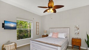 A bedroom with a bed, a ceiling fan, a TV, a window with a view of trees, and a nightstand with a lamp. - 5*Star Coral Falls, 2BR Condo, Naples FL USA, 15min drive to many beaches, shops (Naples)