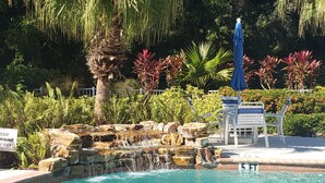 A pool with a waterfall feature, surrounded by lush greenery and a bench area. - 5*Star Coral Falls, 2BR Condo, Naples FL USA, 15min drive to many beaches, shops (Naples)