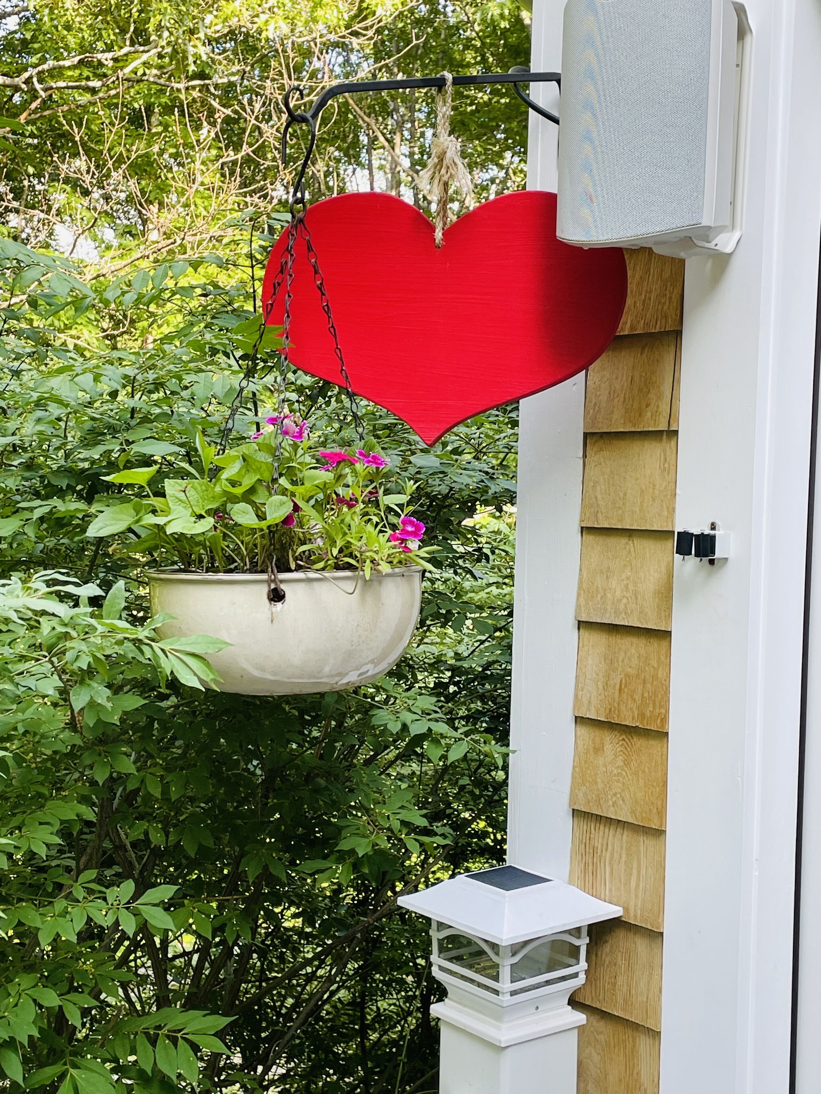 A hanging planter with a heart-shaped top, a white birdhouse, and dense green foliage.