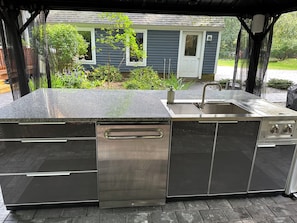Una cocina exterior con un lavamanos de acero inoxidable, horno empotrado y lavavajillas.