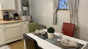 A dining area with a table set for two, a coffee machine, and a window with curtains. - Cozy Apartment (sleeps 6) (Kodak)