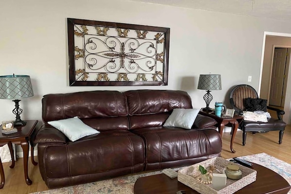 A living room with a brown leather sofa, two side tables with lamps, a decorative wall piece, and a chair.