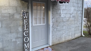 A house with a gray door, a 'WELCOME' sign, and a red awning. - Cozy Apartment (sleeps 6) (Kodak)