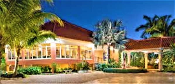 Um hotel com fachada de vidro ampla, palmeiras e área externa coberta.