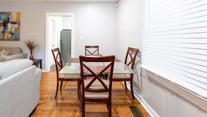 A dining area with a glass table, wooden chairs, and a grey sofa.