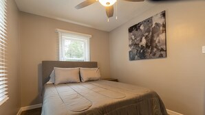A bedroom with a bed, a ceiling fan, a window with blinds, and a painting on the wall.