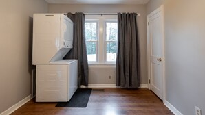 A laundry room with a washer and dryer, a window with curtains, and a door.