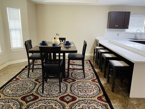 Una cocina moderna con comedor, que cuenta con una isla grande, sillas de madera oscura y alfombras estampadas.