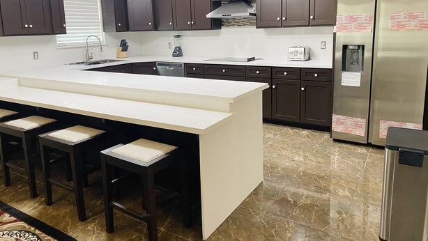 A modern kitchen with dark cabinets, a white countertop, and a stainless steel refrigerator.
